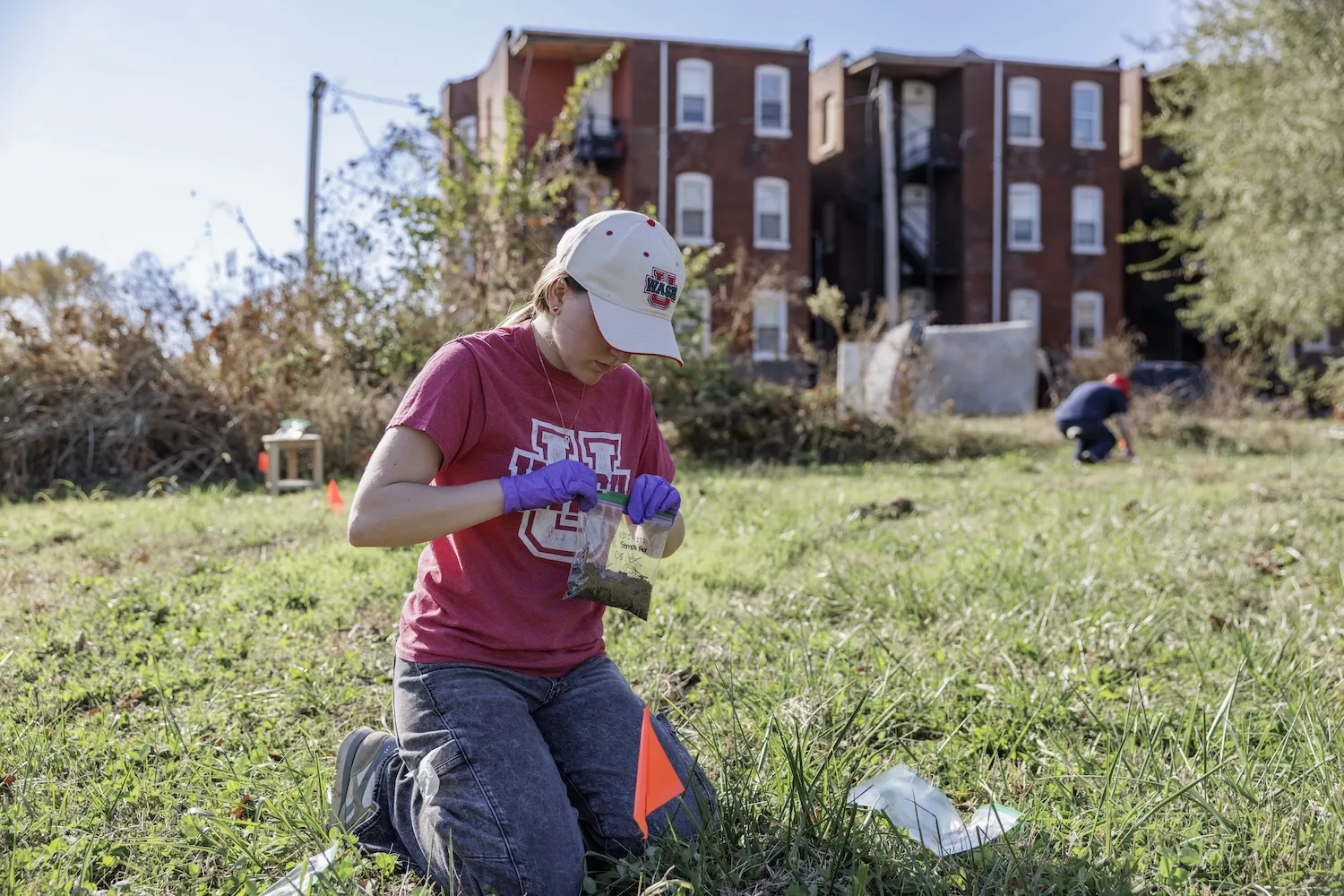 A woman kneels while collecting soil samples.
