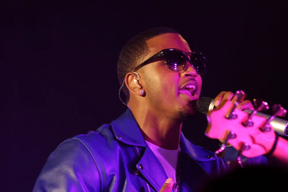 A man wearing sunglasses sings into a microphone.