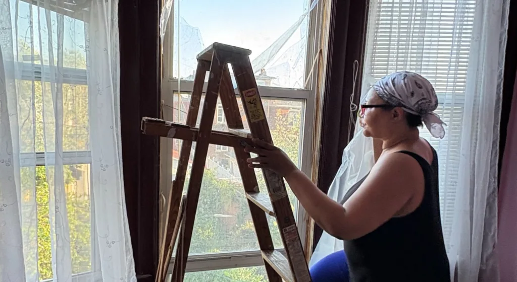 A woman on a ladder looks out the window.