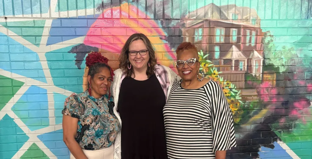 Three women stand before a mural