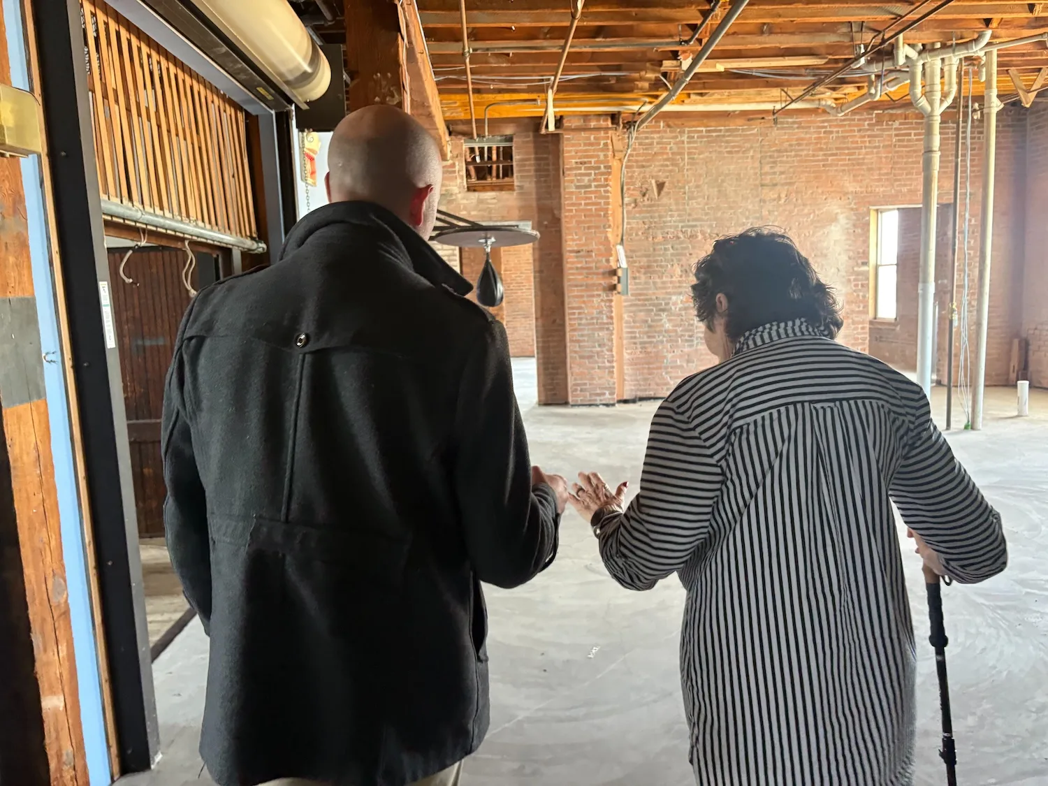 A young man helps an older woman who is walking with a cane.
